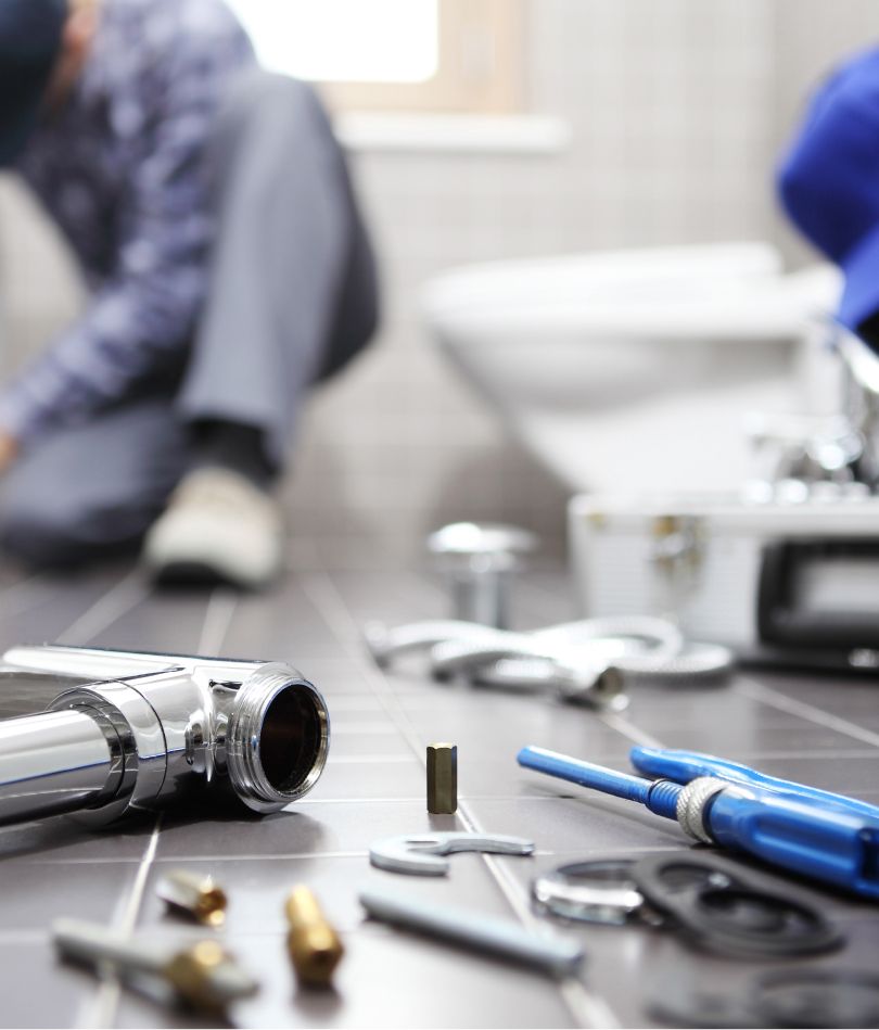 Professioneller Installateur bei der Reparatur im Badezimmer, mit Werkzeugen und Sanitärmaterialien auf dem Boden verteilt, symbolisiert Kompetenz in Badsanierung, Heizungstechnik und der Wartung von Anlagen für erneuerbare Energien durch Bad + Heizung André Haar in Höxmark.